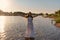 An immature young girl in a white wet dress is standing in a river and sprinkles water droplets up in the rays of the rising sun