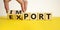 Import or export symbol. Hand is turning a cube and changes the word `import` to `export`. Beautiful yellow table, white