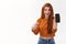 Impressed attractive millennial redhead female in cropped sweater, holding smartphone, pointing mobile screen and