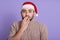 Impressed bearded man looking directly at camera with shocked look, wearing red santa claus hat and warm beige sweater, being very