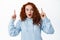 Impressed redhead girl with curly hairstyle pointing fingers up at top advertisement, gasping amazed and stare at camera