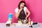 Impressed surprised emotional model poses isolated over pink background, wearing brown apron and white t shirt , talking over her