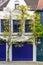 Impressing tree growing around sharply white medieval house with brightly navy blue windows, door and garage door