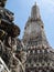 The impressive spire of the Wat Arun Temple, in Bangkok, Thailand, with all its intricate details, is stretching towards a blue
