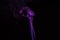Incense stick with purple smoke against black background