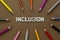 Inclusion word with colorful pencils over brown background. Equality, community integration concept. Top view