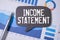 INCOME STATEMENT text on sticky with pen ,calculator and glasses on beige background