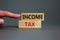 Income tax symbol. Concept words `income tax` on wooden blocks on a beautiful grey backgrounds. Businessman hand. Business, inco