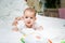 Increased salivation in the infant during teething. A baby girl in white clothes is lying on a white bed, smiling, drooling.