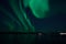 Incredible strong aurora borealis over fjord and snowy mountain