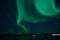 Incredible strong aurora borealis over fjord and snowy mountain