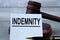 INDEMNITY - word on a white sheet against the background of a judge\\\'s hammer and a wooden stand