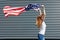 Independence day and patriotic concept. Active girl with long ginger hair running with waved by wind USA flag, holding it above.