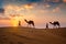 Indian cameleers camel driver with camel silhouettes in dunes on sunset. Jaisalmer, Rajasthan, India