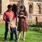 Indian couple posing for maternity baby shoot with their 5 year old kid. The couple is posing in a lawn with green grass and the