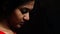 An indian female staring down in worry and depression in black background with selective focus on nose