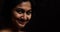An indian female staring and smiling at the camera in black background