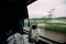 An Indian guy sleeping with food and newspaper while a train moving with green tree motion blur in the outside.