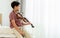 Indian handsome teenage boy, playing, practicing violin musical instrument with happiness in bedroom at cozy home in leisure time