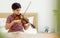 Indian handsome teenage boy, playing, practicing violin musical instrument with happiness in bedroom at cozy home in leisure time