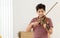 Indian handsome teenage boy, playing, practicing violin musical instrument with happiness in bedroom at cozy home in leisure time