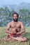 Indian man meditating in lotus yoga pose on green grass in Kerala, South India