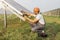 Indian man sitting near solar panel with multimeter in hands