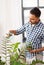 Indian man spraying houseplant with water at home