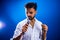 Indian man in white shirt with beard singing in recording studio on blue background