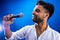 Indian man in white shirt with beard singing in recording studio on blue background