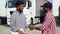Indian manager and african trucker shaking hands by truck