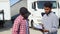 Indian manager and african trucker standing by truck with a clipboard, checking the delivery list. Two workers preparing
