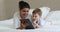 Indian mother and little Caucasian son using tablet on bed