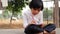 Indian schoolgirl is sitting on the stone in the park and writing in a book. A little girl is doing her homework in nature