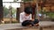 Indian schoolgirl is sitting on the stone in the park and writing in a book. A little girl is doing her homework in nature