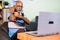 indian senior old man massaging hand using wood roller massager by watching online medication videos on laptop from home