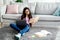 Indian teen girl reading textbook, sitting on floor with laptop and study materials, learning remotely from home