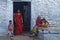 Indian woman sits in front of the doorstep of her house  while her young daughter stands in the entrance of the house