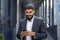 Indian young male businessman standing on the street near an office building and using a mobile phone, dialing a number