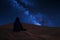 individual sitting on dune, observing starry night