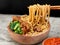 Indonesian chicken noodles called mie ayam topped with chicken meat and green mustard served in a bowl with red spicy sauce