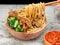 Indonesian chicken noodles called mie ayam topped with chicken meat and green mustard served in a bowl with red spicy sauce