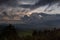 Indonesian landscape with rainy sky on sunset - dark blue clouds with orange, yellow sunbeams over hazy mountains, smoky green.