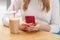 Indoor cropped picture of unrecognizable woman holding her smartphone in both hands, sitting at table, having plastic cup of