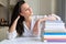 Indoor image of young woman posing at home with her reading stack of books. Smart female student rests on stack of books.