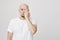 Indoor portrait of focused and determined bald bearded caucasian male squinting with one eye while covering half of face