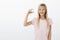 Indoor portrait of happy satisfied adorable young girl with fair hair, looking at tiny thing, shaping it with fingers