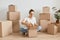 Indoor shot of adorable delighted female in white t-shirt packing cardboard box, woman packing things to move among carton parcels