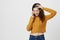 Indoor shot of adult woman talking on phone while touching head and being shy or nervous, smiling and looking on