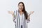 Indoor shot of amazed and thrilled happy woman in eyewear and striped blouse, spreading palms in joy and smiling broadly